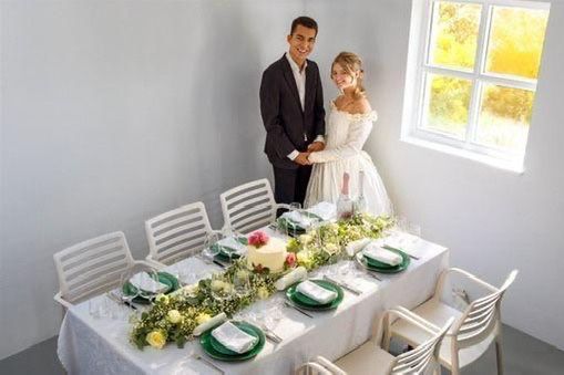 Bruid en bruidegroom staan naast een versierde tafel voor de huwelijksreceptie in een lichte, witte ruimte.