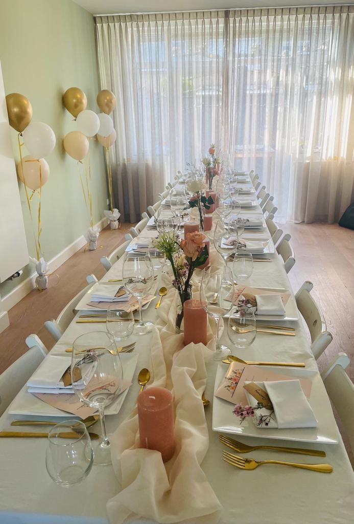 Een lange feesttafel, elegant gedekt met kaarsen, gouden ballonnen en doorschijnende gordijnen