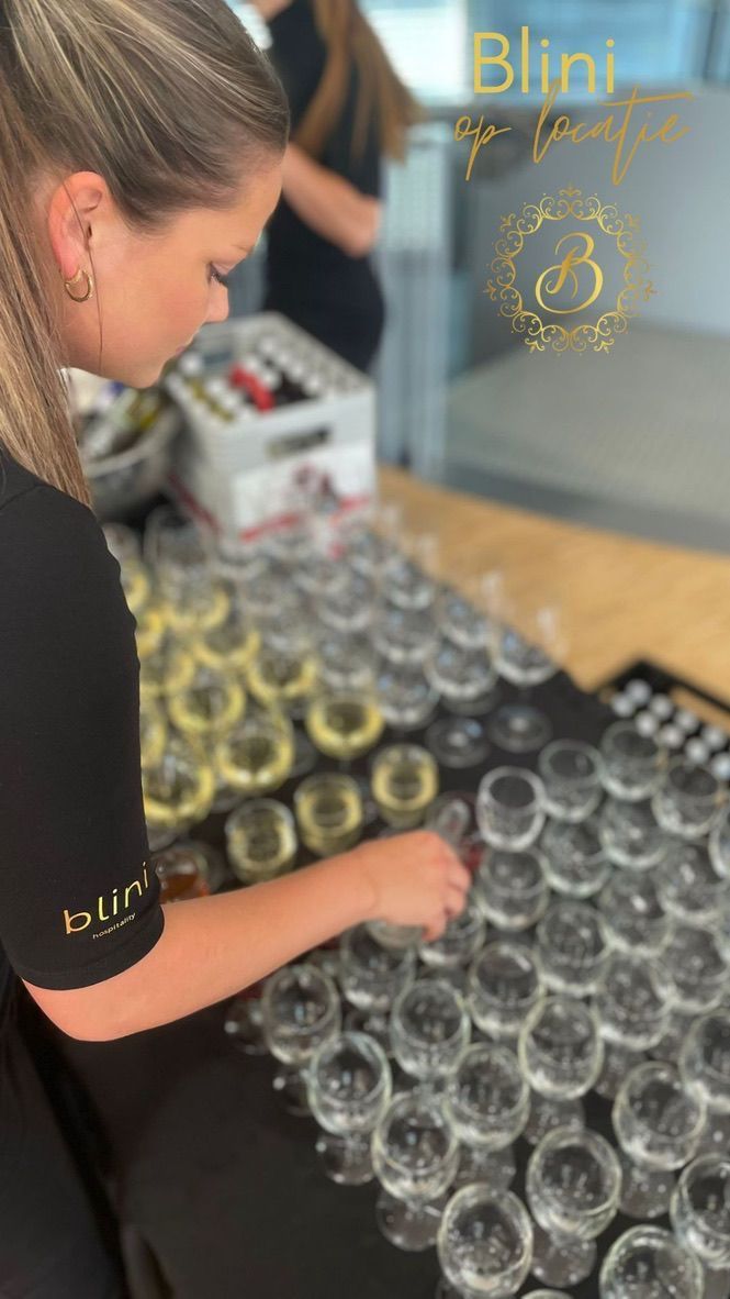 Vrouw schikt rijen glazen op een houten tafel naast een gouden bord met het
