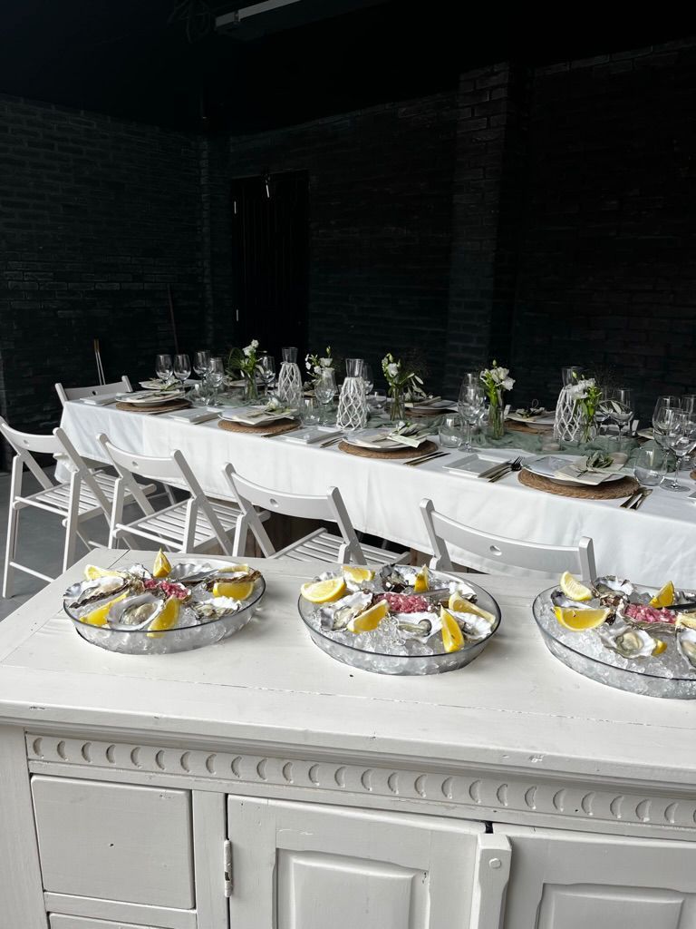 Elegante eettafelset voor buiten met witte stoelen, glaswerk en gedecoreerde gerechten in een donkere patio-omgeving.