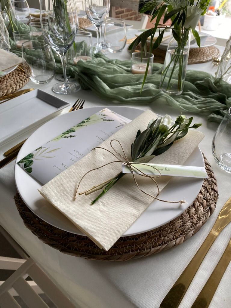 Een elegante tafelsetting met geweven onderborden, gevouwen servetten en groene tafelstukken voor een formeel evenement.