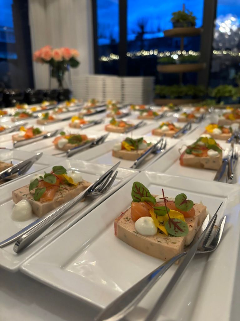 Op een feesttafel, bij een raam in de schemering, staan op bordjes met hapjes, geserveerd met een tang.