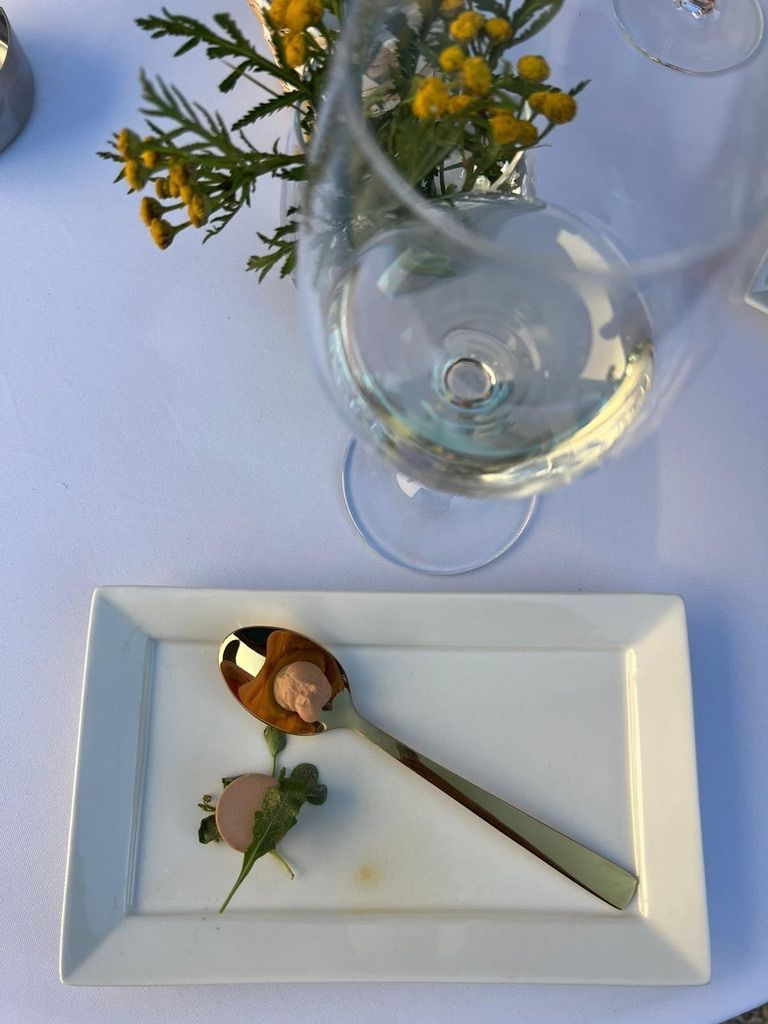 Een elegant gedekte tafel met een wijnglas, wit bord, lepel en een kleine bloemversiering op een blauw tafelkleed.