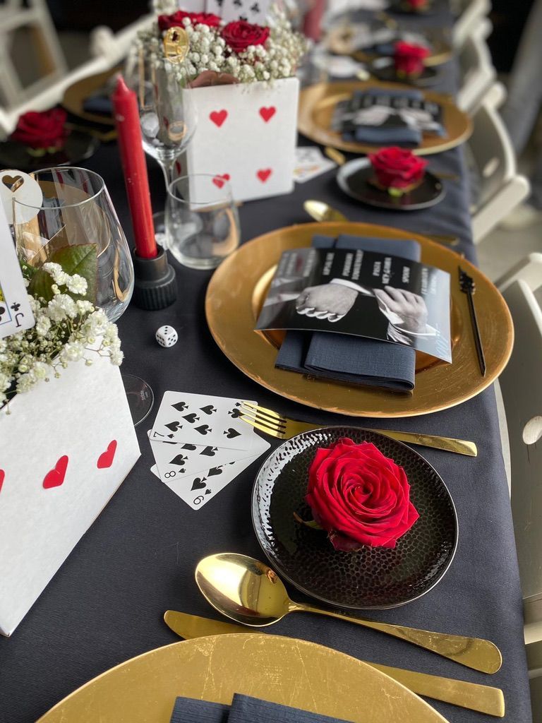 Een elegante zwart-gouden tafelsetting met rozen, speelkaarten en kaarsen op een formele eettafel.