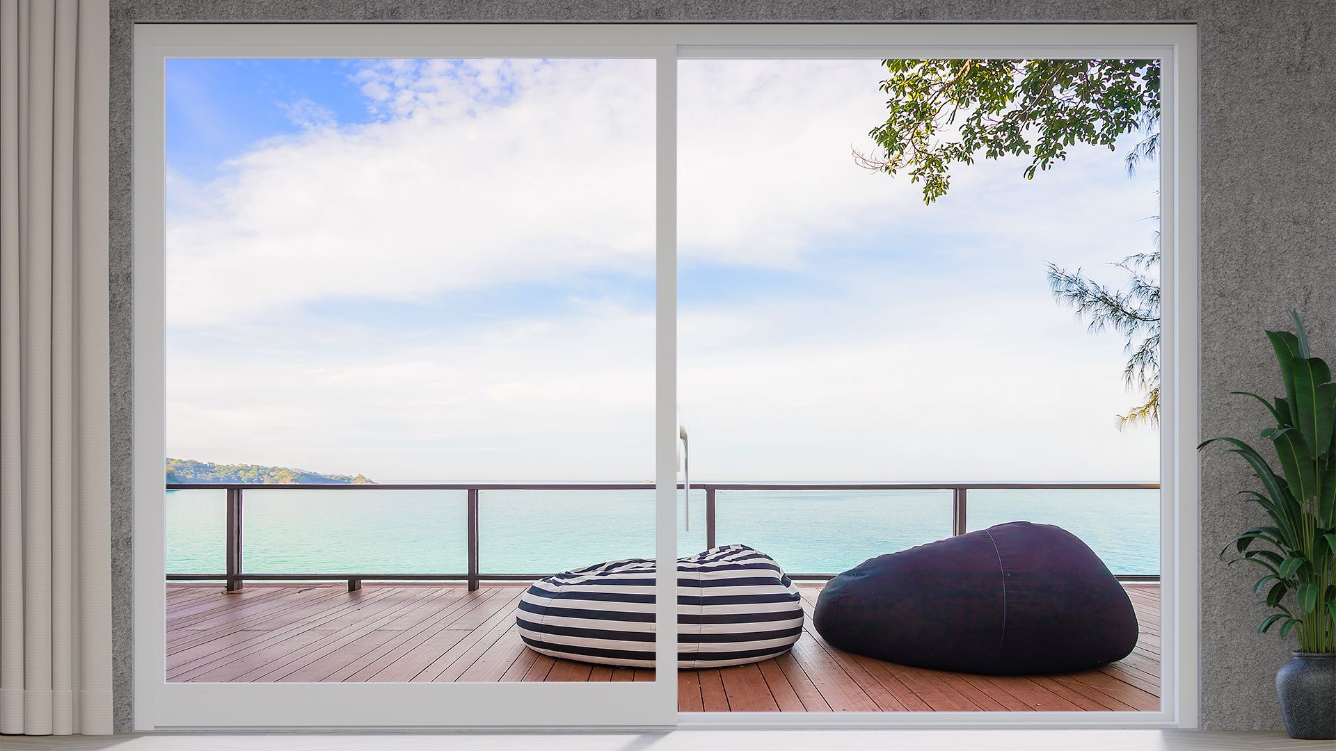 Camera moderna con ampia finestra affacciata su un patio sul mare, pouf e vista sull'oceano.