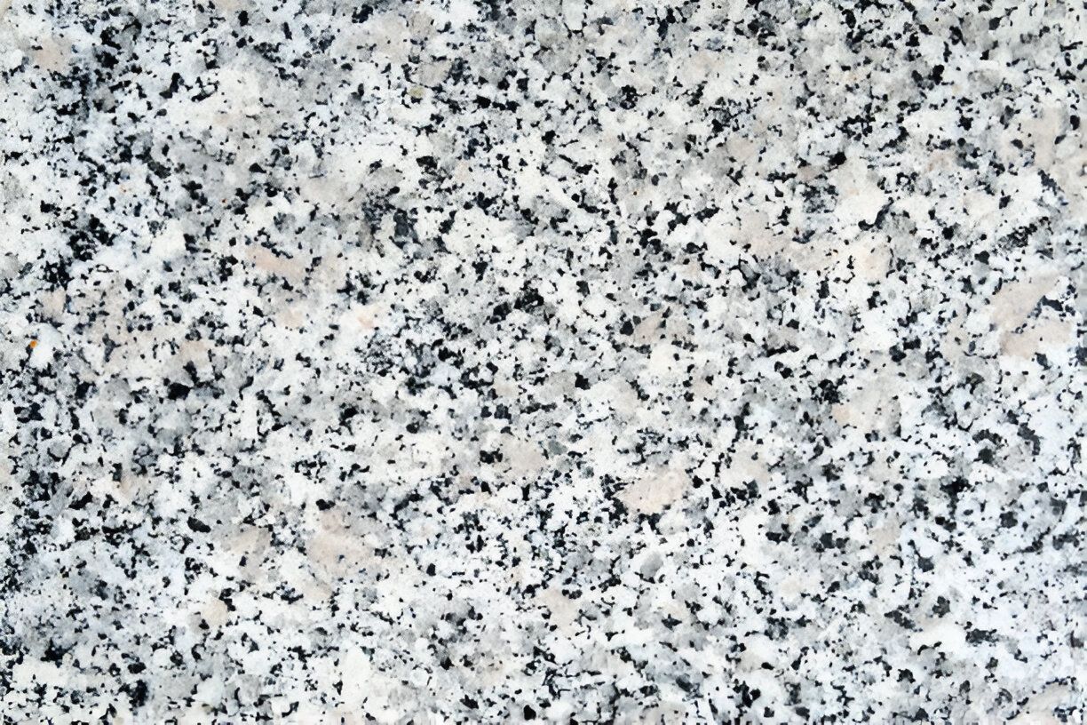 A close up of a white granite counter top with black spots.