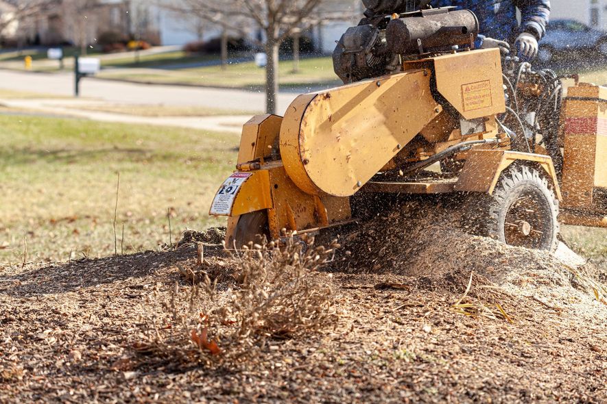 Worker using a yellow wood chipper to clear leaves on a grassy curbside.