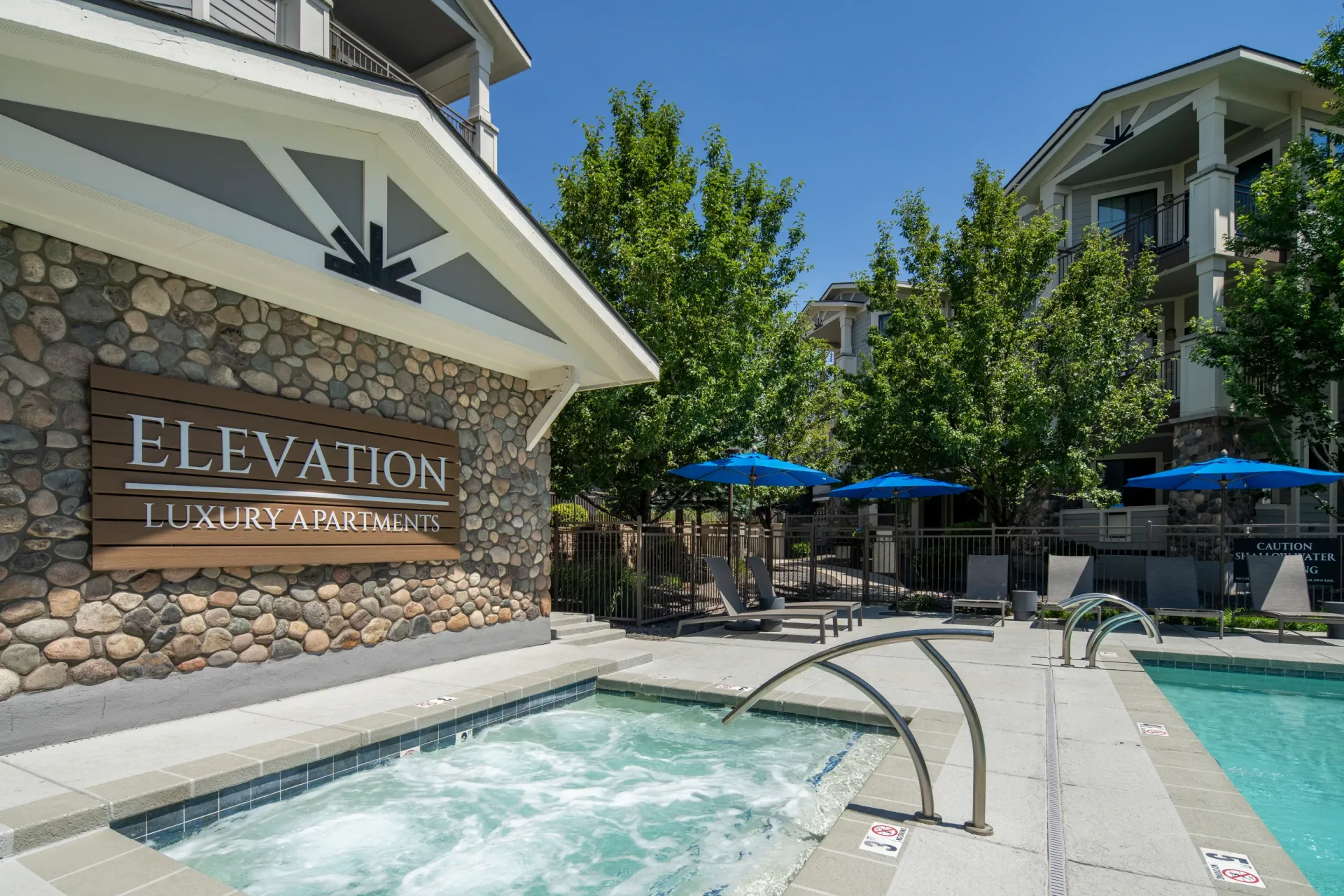 Elevation Luxury Apartments exterior sign and outdoor pool area with hot tub and lounge chairs.
