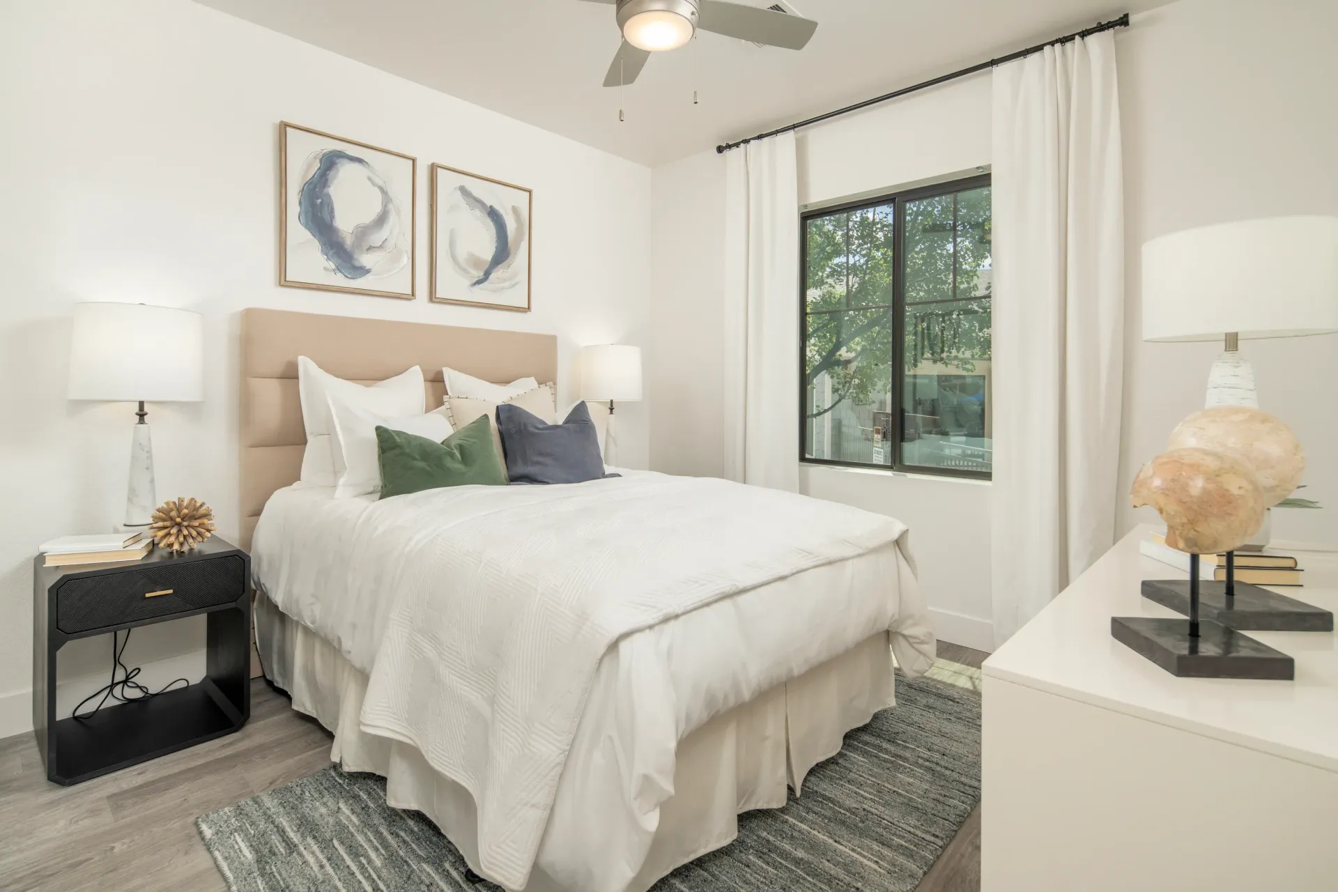 A cozy bedroom featuring a queen-size bed with white linens, green and blue accent pillows, and two framed abstract artworks on the wall at Elevation in Flagstaff, AZ.