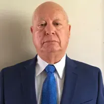 Man in a blue suit and tie standing against a plain light background