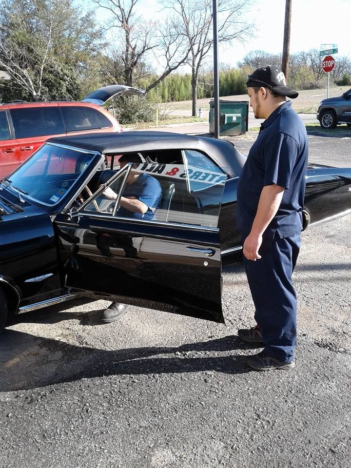 Man standing beside a black classic car with its driver door open on a sunny street