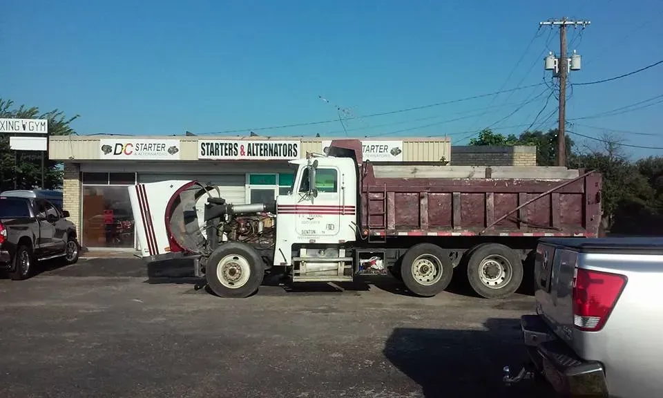 White semi-truck with maroon dump trailer parked in a lot outside a commercial building on a sunny day