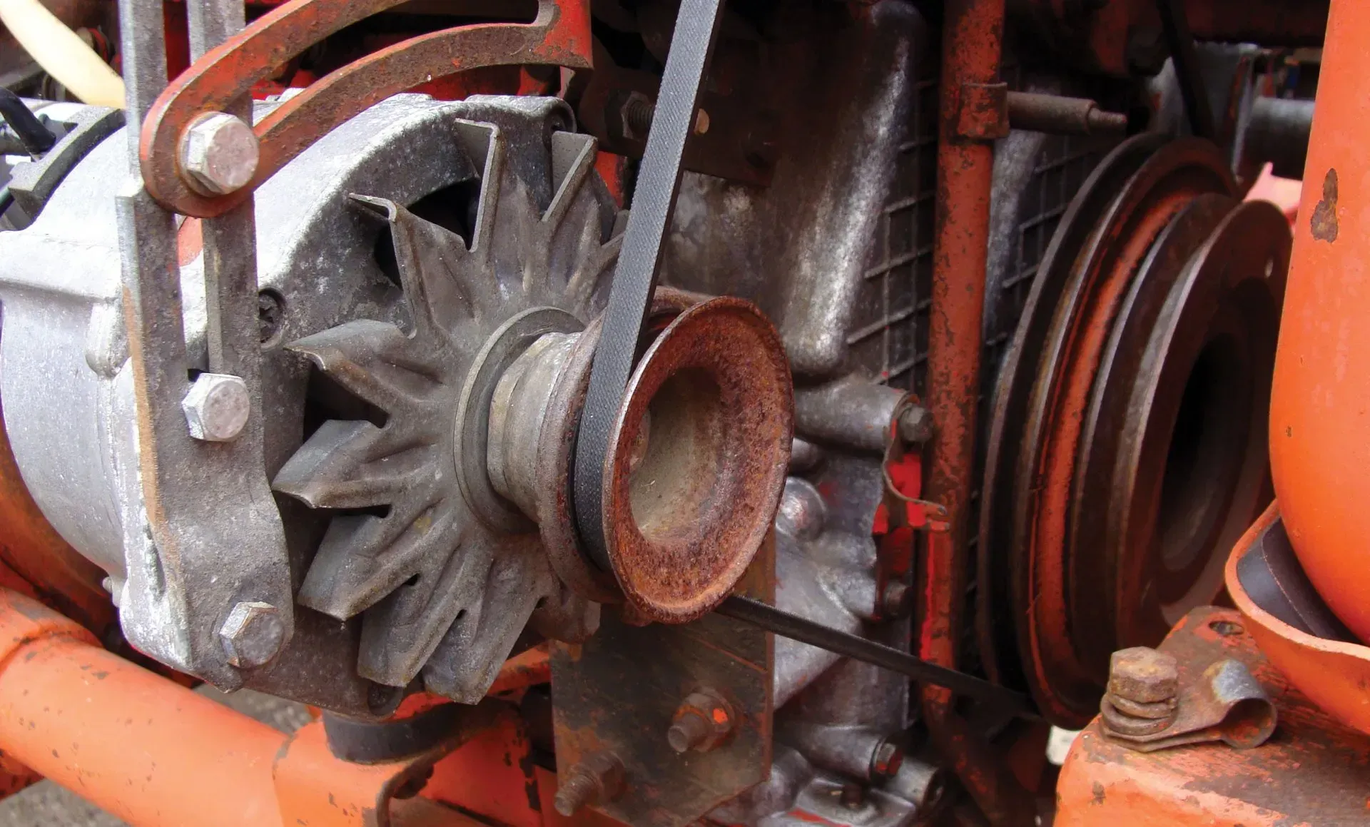 Close-up of rusty mechanical parts with pulleys, gears, and an orange casing inside a machine