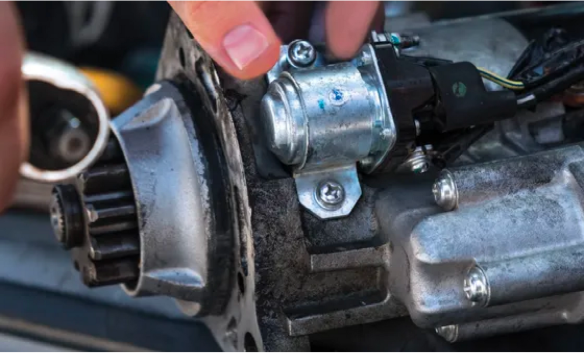 Close-up of a mechanic’s hand pointing to a car engine part with a metal connector and hoses