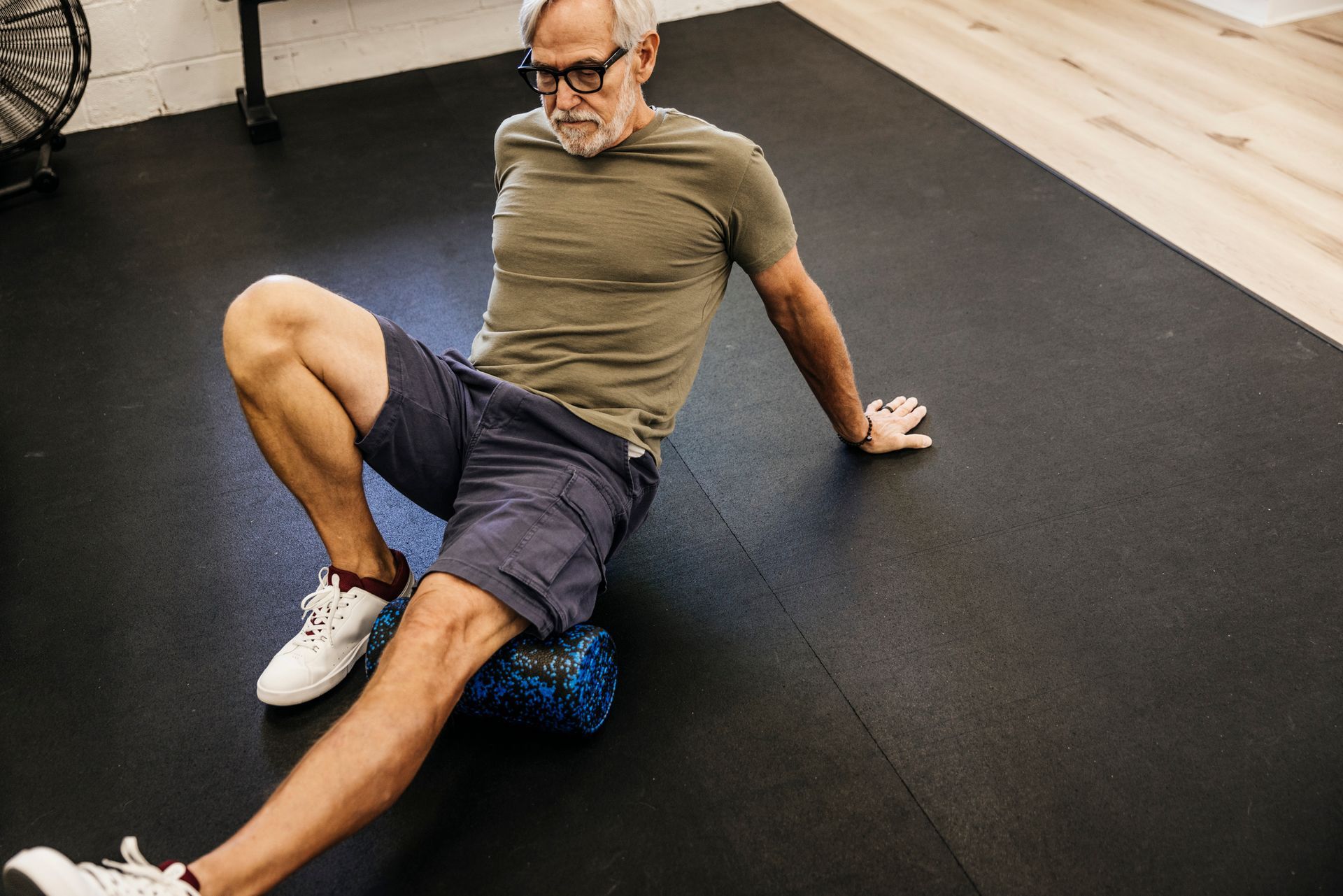 Un uomo è seduto sul pavimento e usa un foam roller sulla gamba.