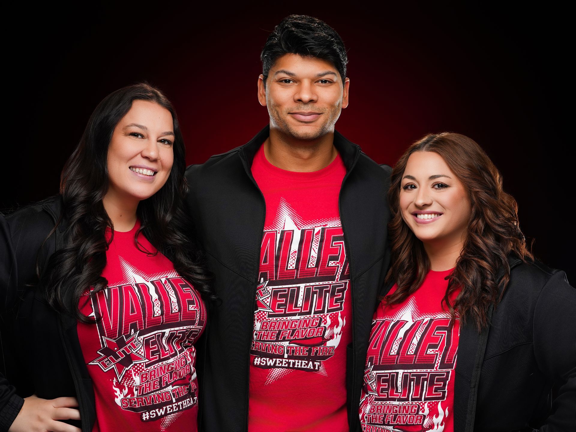 Three people smiling against a red backdrop, wearing matching red shirts with 