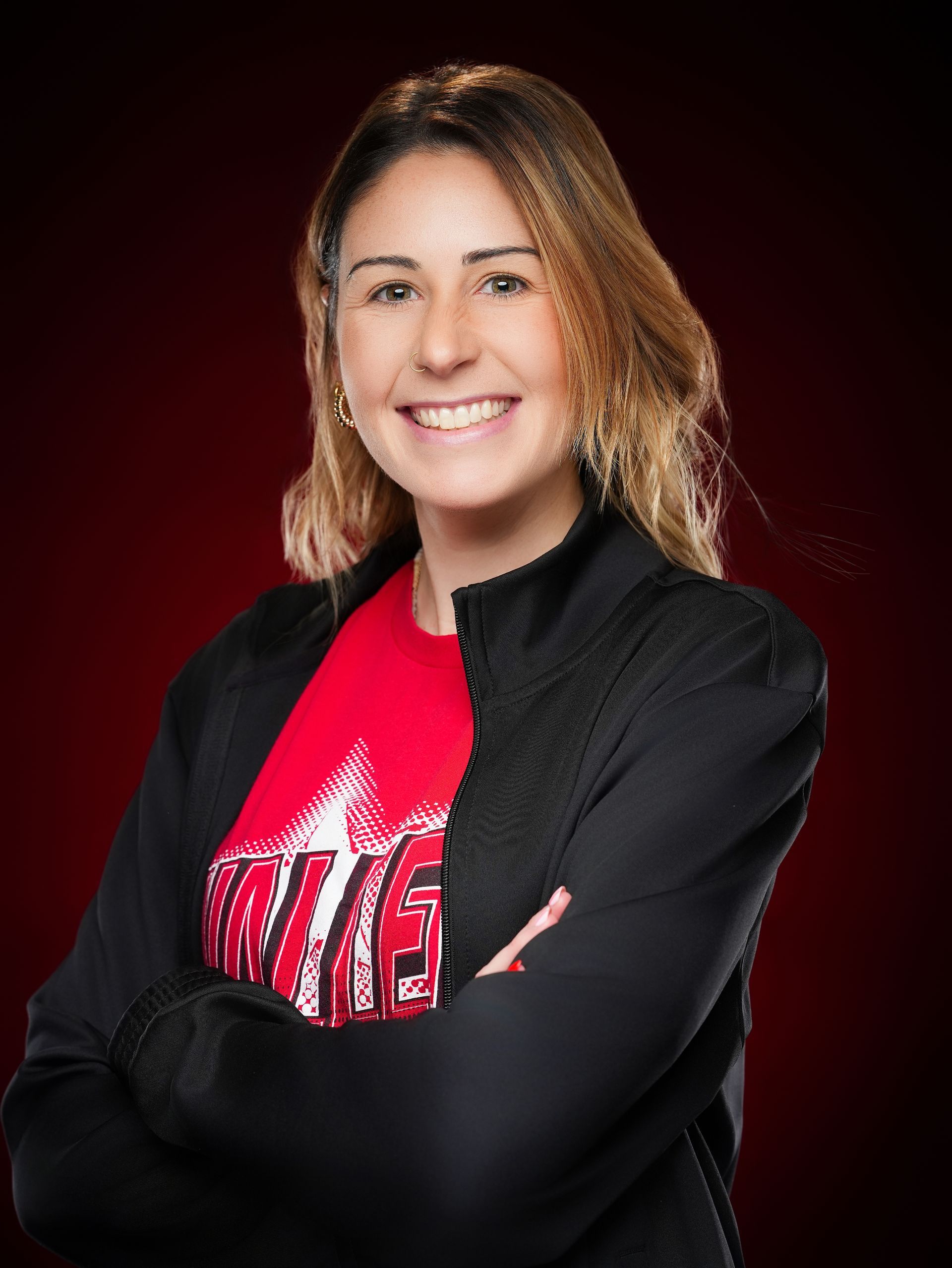 A smiling person with shoulder-length hair wearing a red graphic t-shirt
