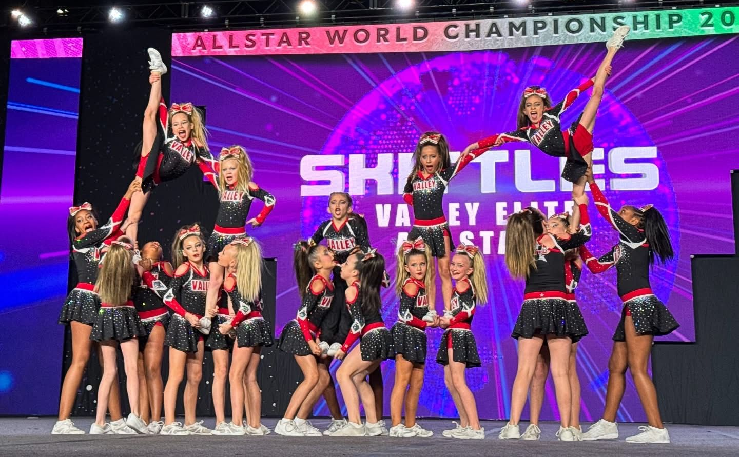 A cheerleading squad in black and red uniforms performs a routine on a stage at the Allstar World Championship.