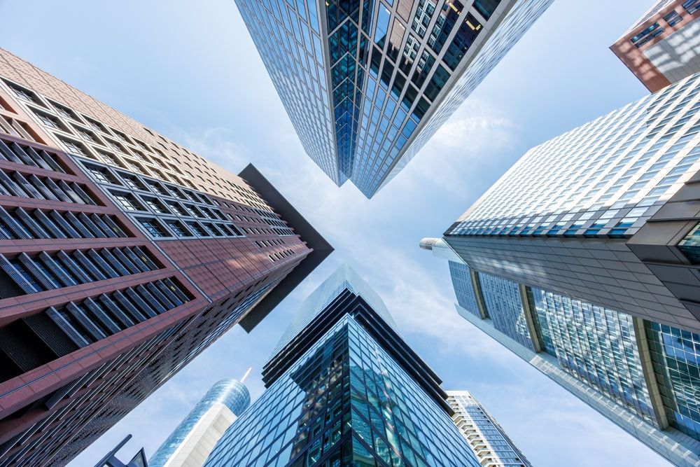 Low-angle view of four tall skyscrapers against a blue sky. Buildings have glass and brick facades.