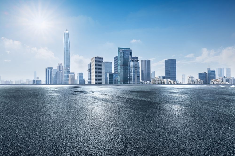 City skyline with skyscrapers under a bright blue sky, viewed from a wet asphalt surface.