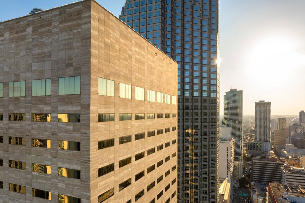 Skyscrapers in a city, with one building featuring horizontal rows of windows reflecting sunlight.