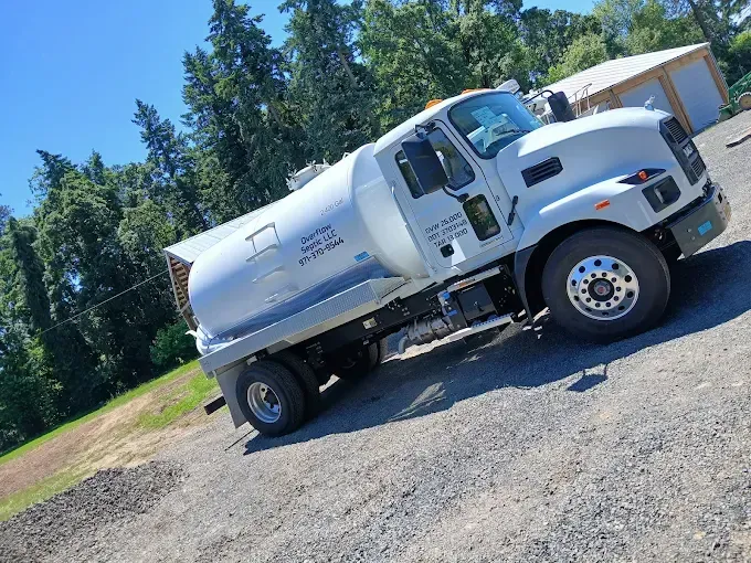 White water tanker truck parked on gravel, trees and blue sky background.