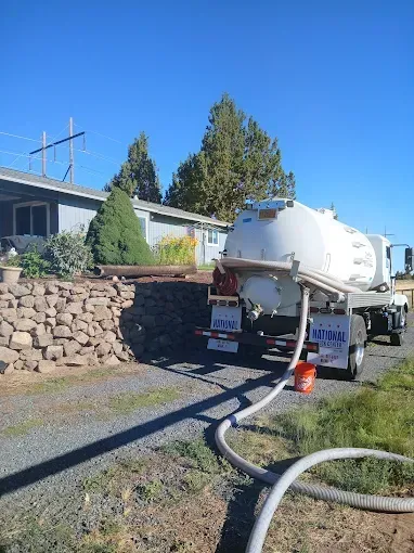 Septic tank truck servicing a house; white tank and hose visible.