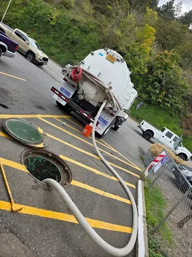 Septic tank truck emptying waste into an open manhole on a paved road.