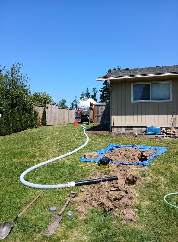 A hose connecting a truck to a backyard excavation, likely for septic tank service. Sunny day.