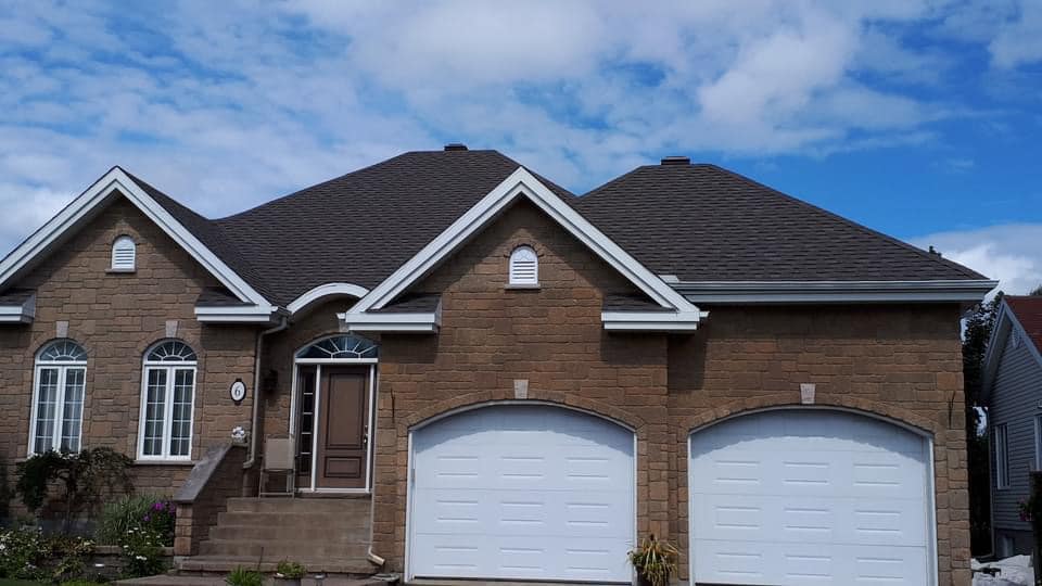 Une grande maison en brique avec deux portes de garage blanches