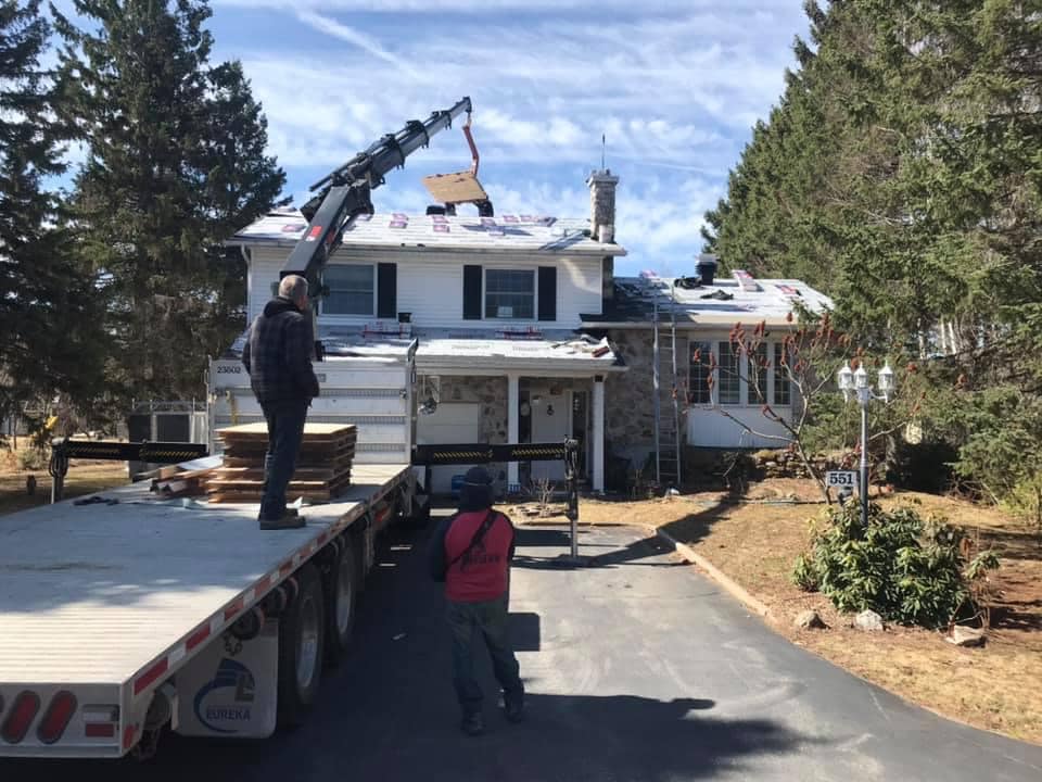 Un homme se tient debout sur un camion à plateau devant une maison.