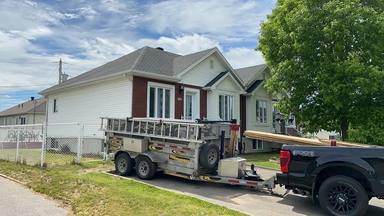 Un camion remorque une remorque avec une échelle devant une maison.