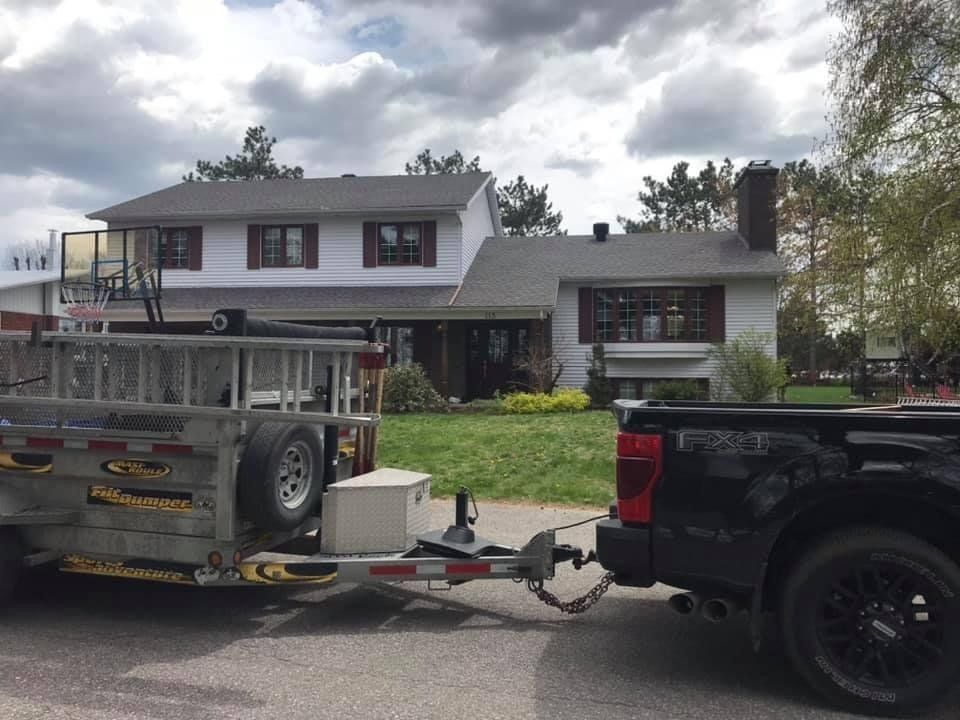 Un camion tire une remorque avec une échelle devant une maison.