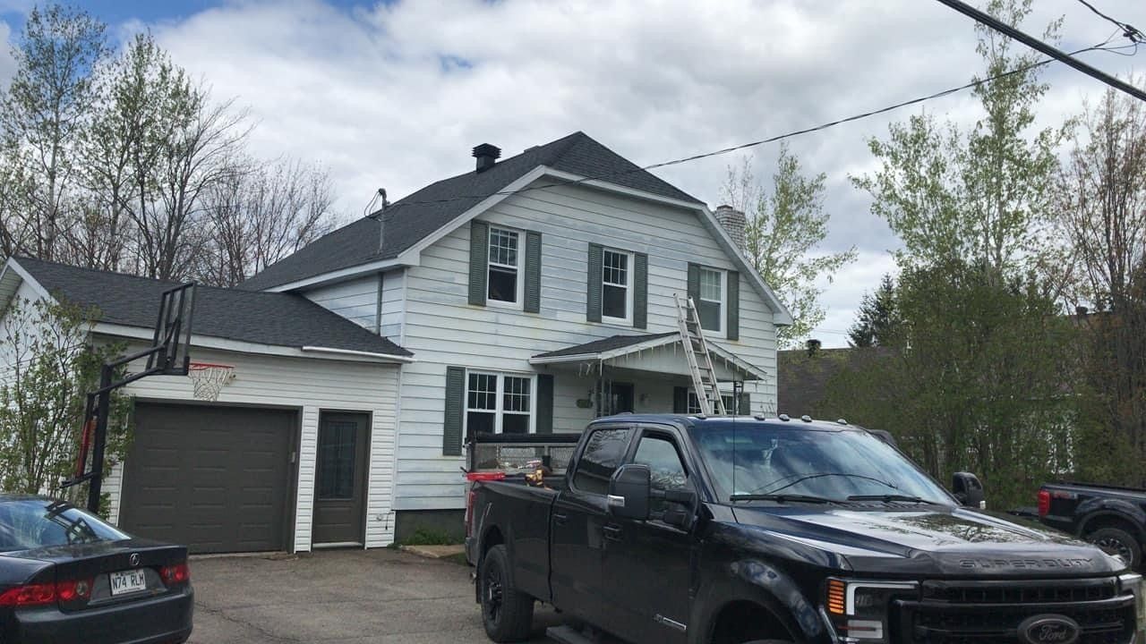 Un camion noir est garé devant une maison blanche.