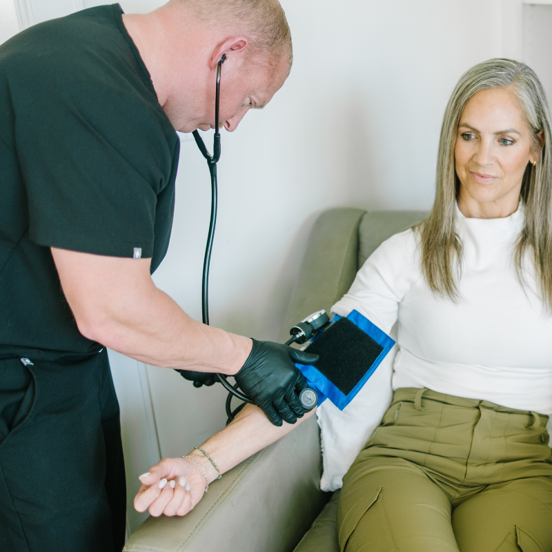 Healthcare worker taking blood pressure on a seated patient with a cuff and monitor in a clinic room