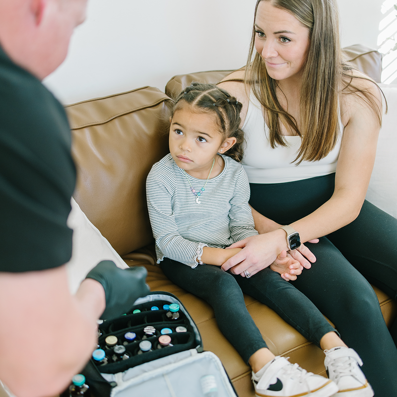 Woman and child sitting on a couch, listening to a person holding a medical kit.