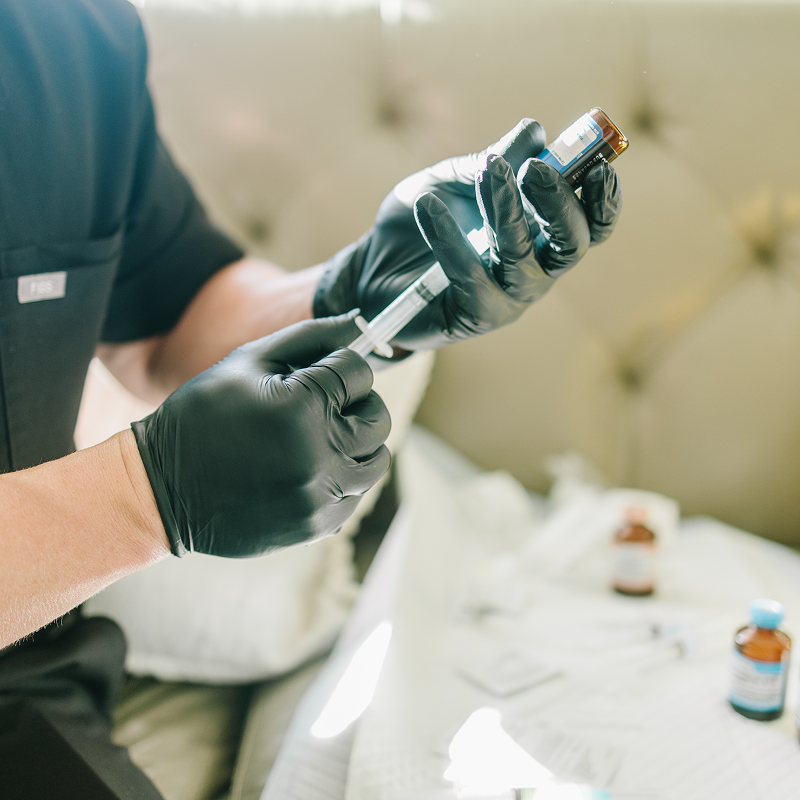 Gloved hands prepare a syringe beside small vials on a medical table.