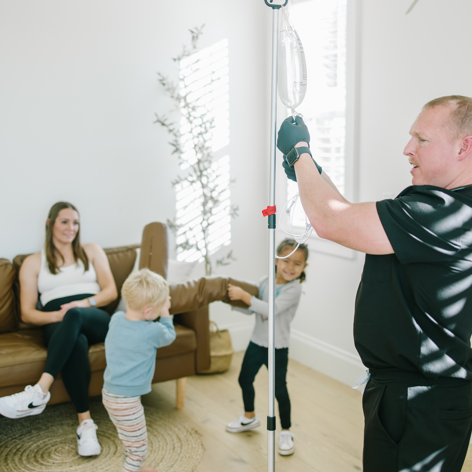 Person hangs IV bag near woman and two children in a bright living room