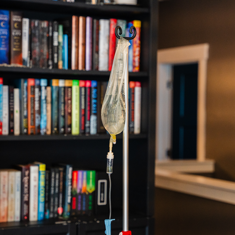 IV bag hanging on a metal stand beside a bookshelf and window