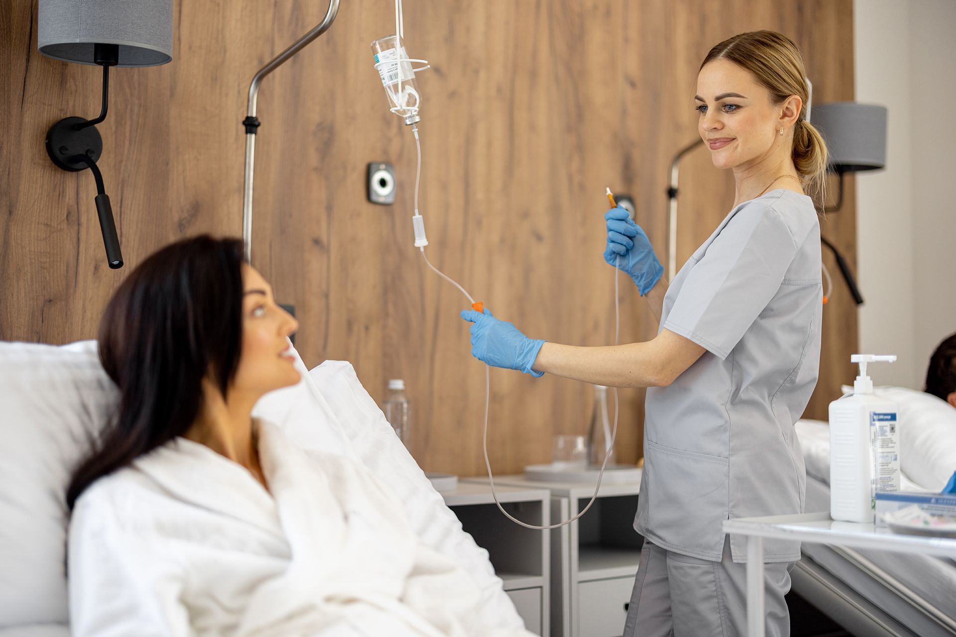 Nurse adjusting IV line beside a smiling patient in a hospital room