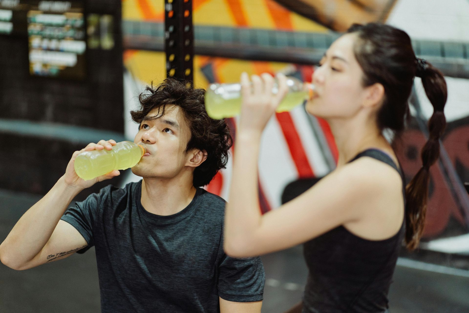 Two people in a gym, drinking sports drinks after workout.