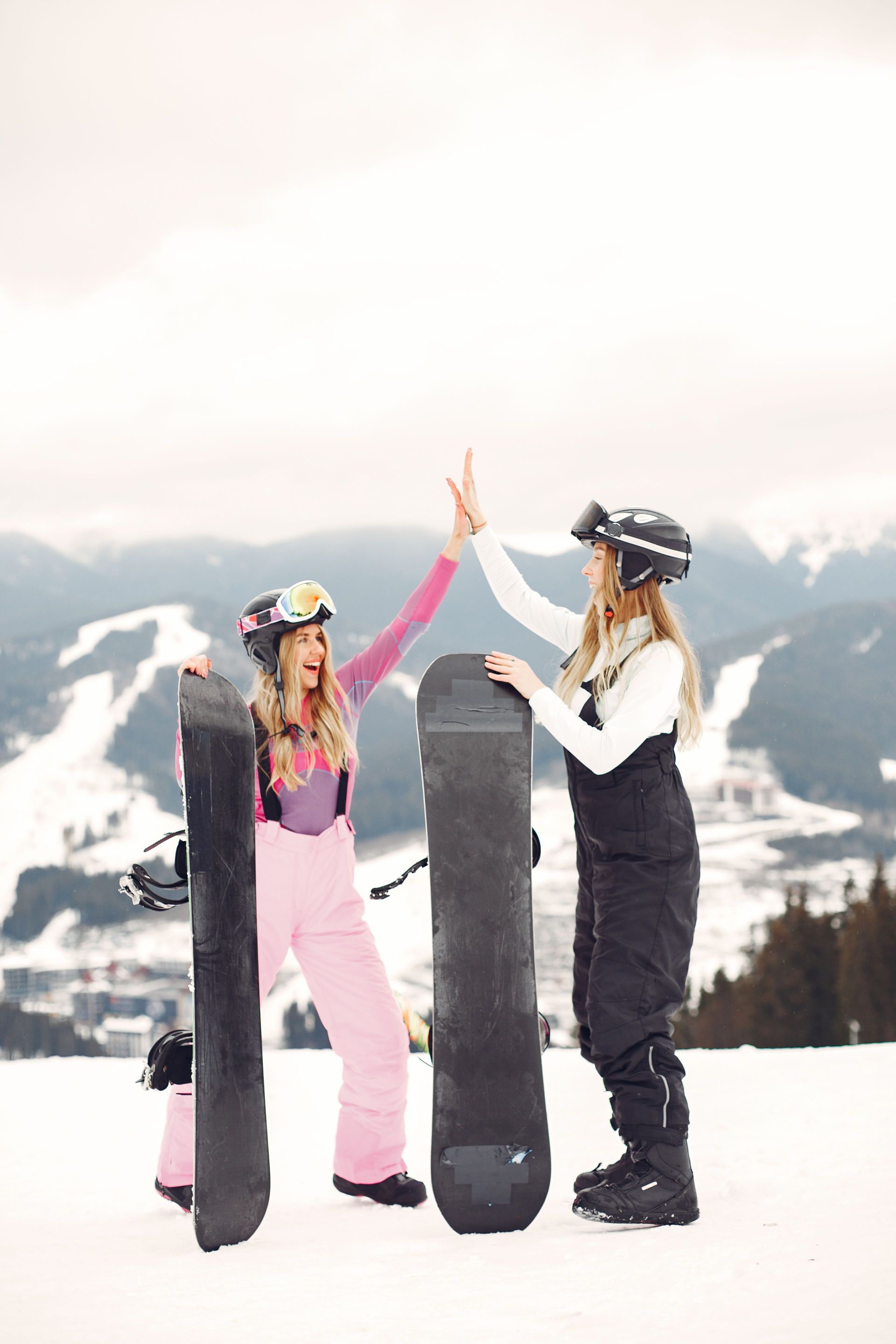 Two snowboarders high-five on a snowy mountain with skis and snowboards in the background