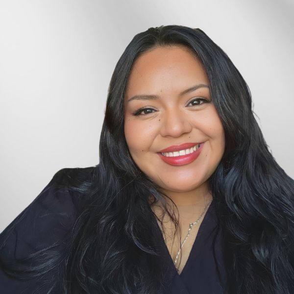 Woman with long black hair smiles broadly, wearing dark top, red lipstick.