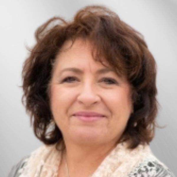 Woman with short, brown curly hair, smiling, wearing a beige scarf, against a blurred background.