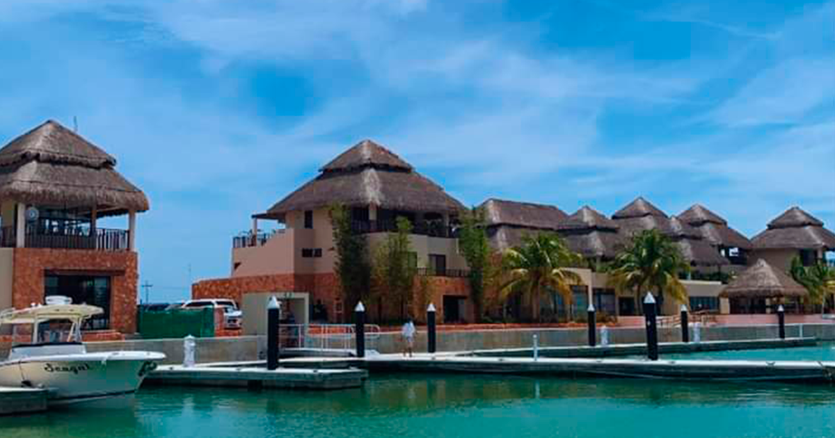 Un puerto deportivo con barcos atracados frente a un edificio con techo de paja.