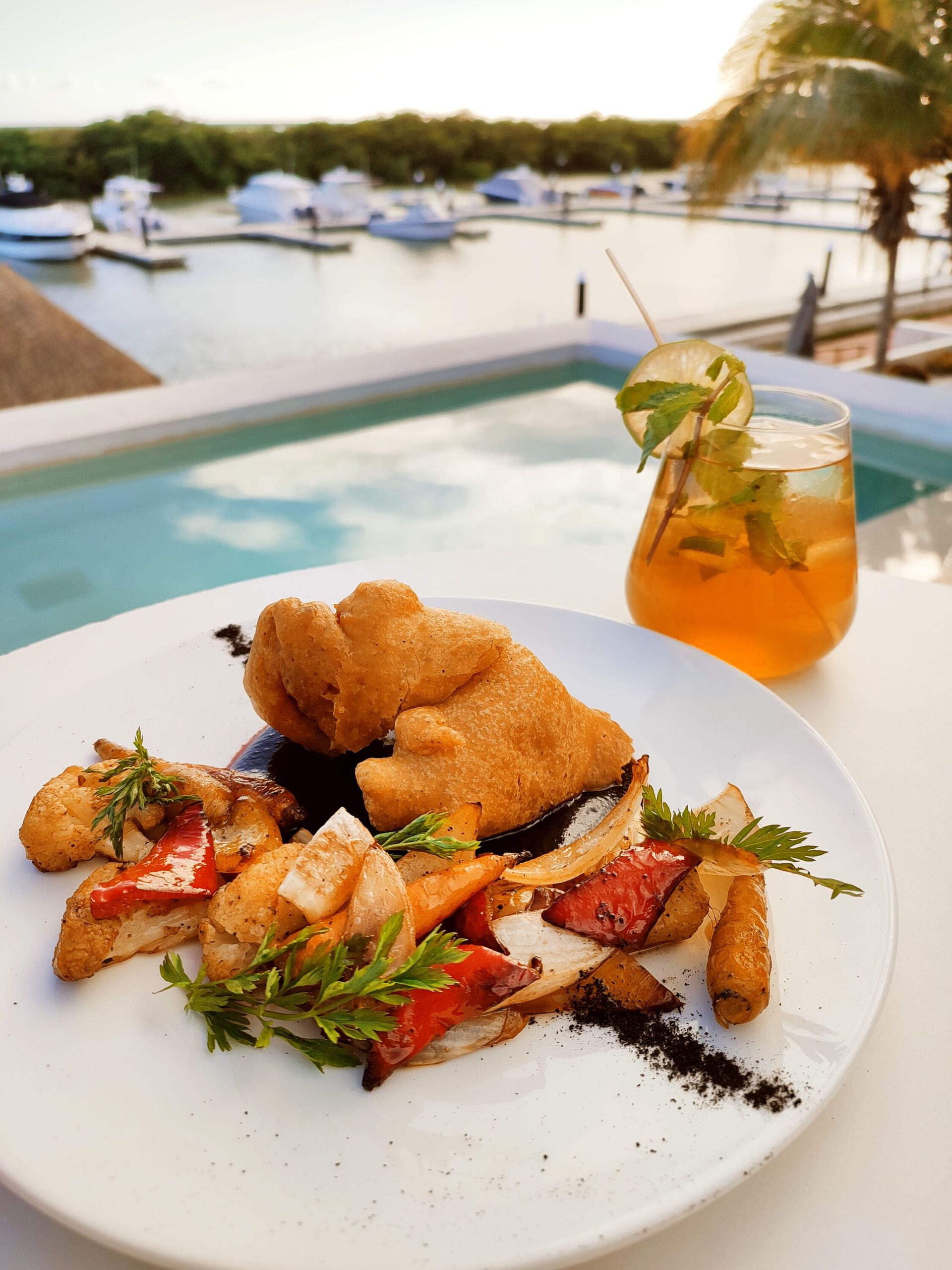Un plato de comida con una bebida frente a una piscina.