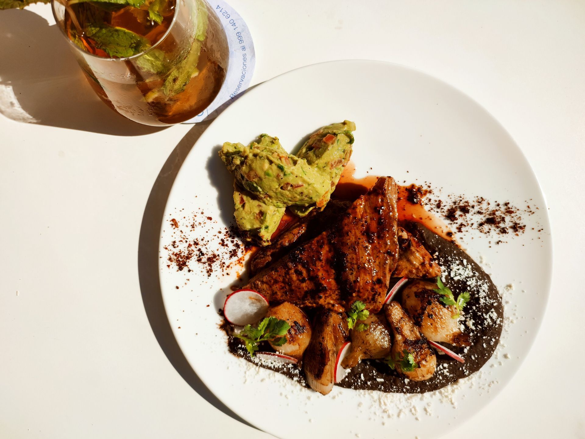 Un plato blanco con carne y verduras junto a un vaso de té.