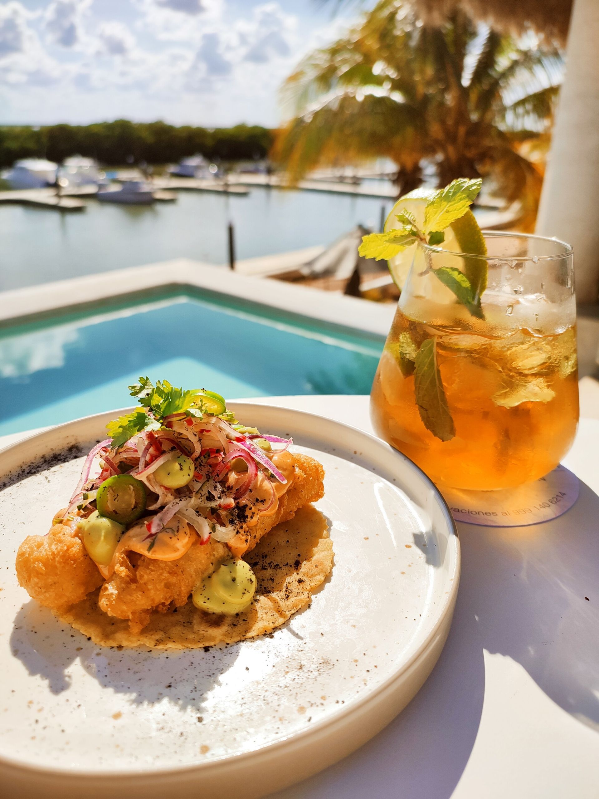Un plato de comida y una bebida están en una mesa al lado de una piscina.