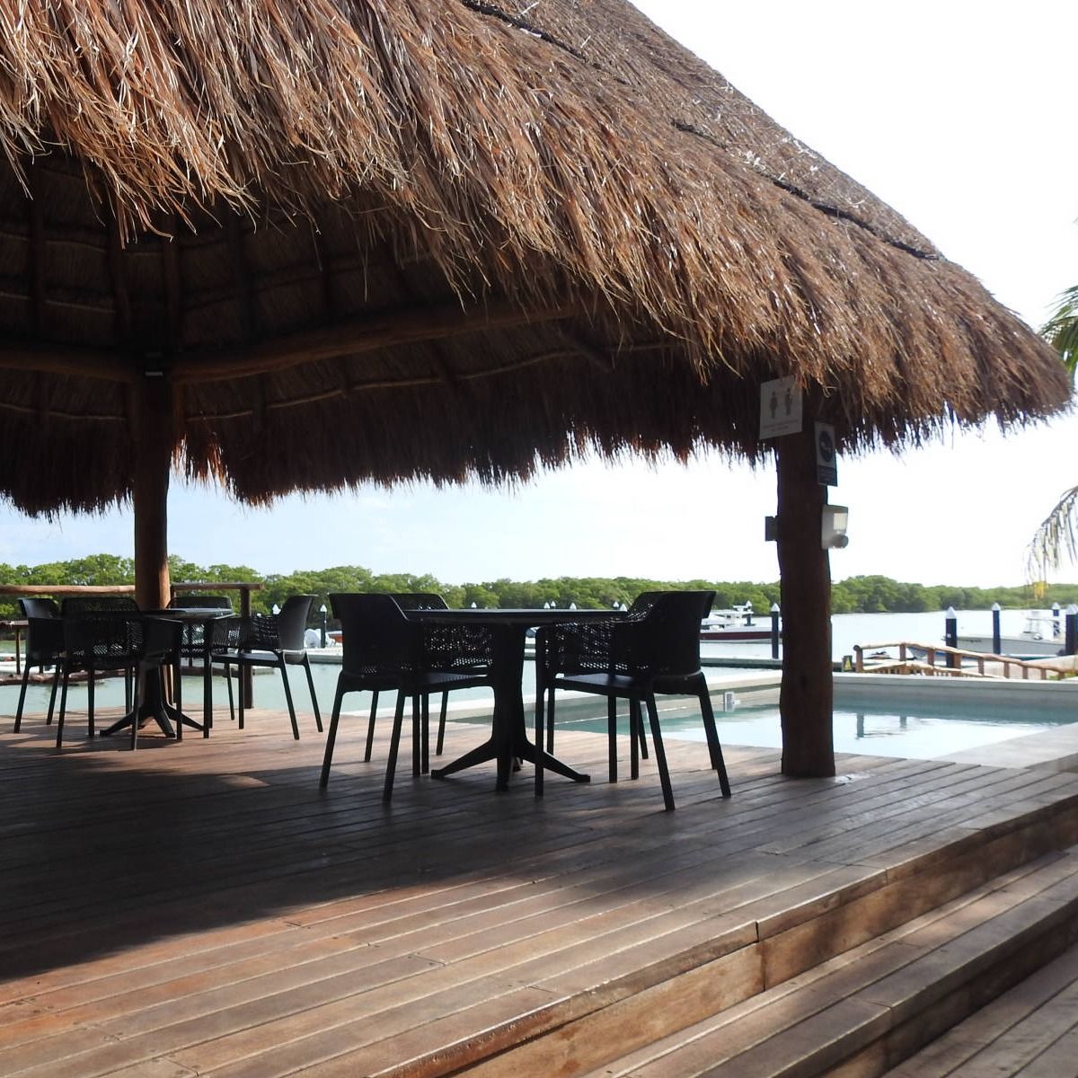 Una terraza de madera con mesas y sillas bajo un techo de paja.