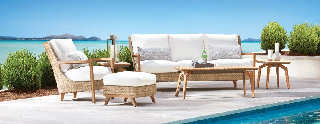 A patio with a couch , chair , table and ottoman next to a pool.